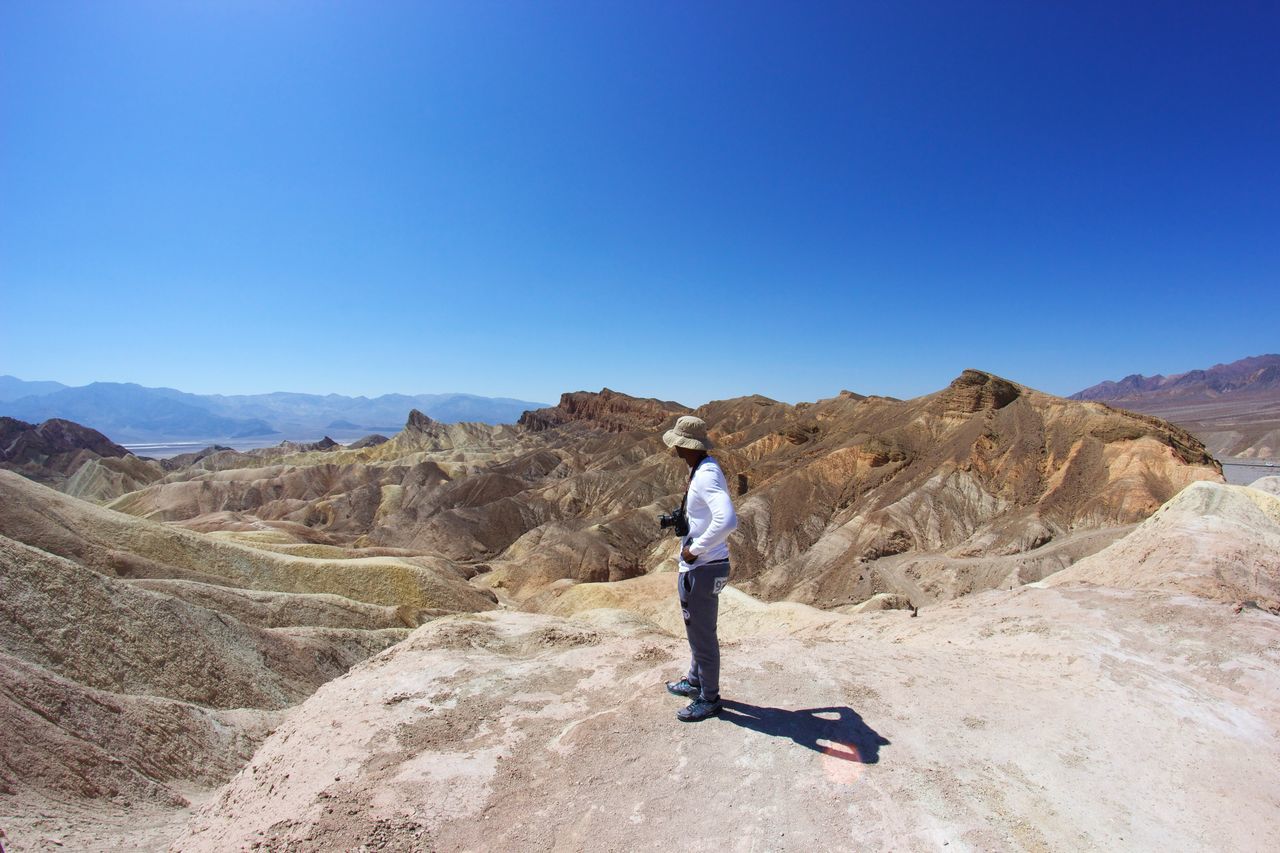 full length, mountain, lifestyles, leisure activity, clear sky, copy space, mountain range, blue, rear view, men, casual clothing, rock - object, standing, landscape, adventure, tranquil scene, hiking, scenics