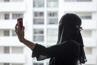 Side view of woman in burka photographing by window in city