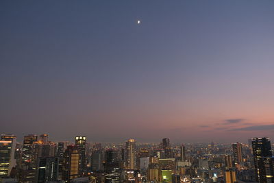 Illuminated buildings in city against clear sky at night