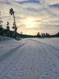 Snow covered field against sky during sunset