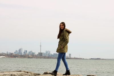 Full length portrait of young woman walking by river with cn tower in background