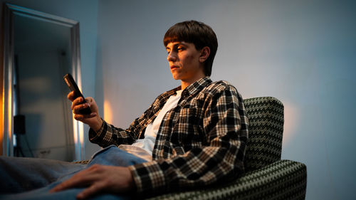 Cool guy sitting in a armchair and browsing on hisr mobile phone at the studio