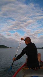 Rear view of man rowing boat at sea against sky