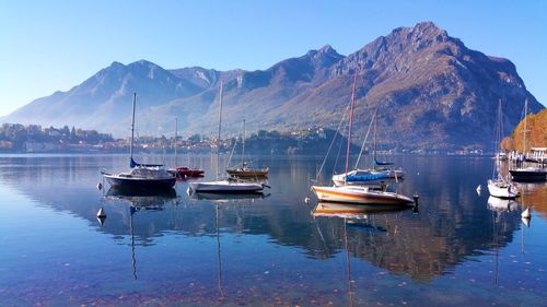 Boats moored in lake with reflections against mountains