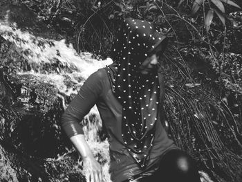 Woman wearing hijab while leaning on rock in forest