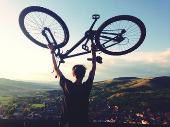 Rear view of man lifting bicycle against mountains