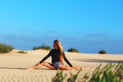 Full length of woman relaxing on sand at beach against sky