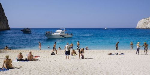 People at beach against clear blue sky