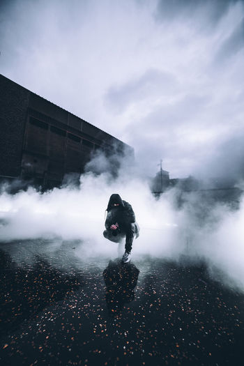 Man wearing hoodie standing amidst smoke on street