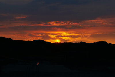 Silhouette landscape against dramatic sky during sunset