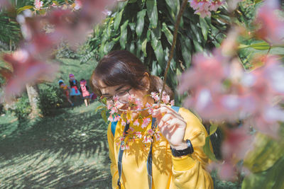 Woman smelling while standing by flowers on tree