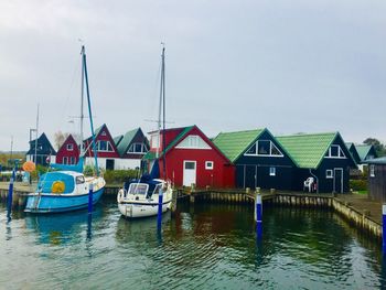 Sailboats moored in river by buildings against sky