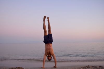 Midsection of man with arms raised on beach against sky during sunset