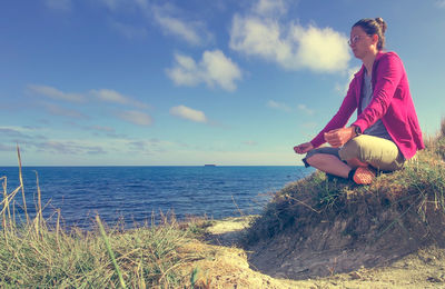 Woman sitting on land by sea against sky