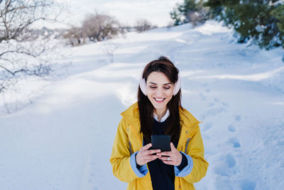 Young woman using phone while standing on snow