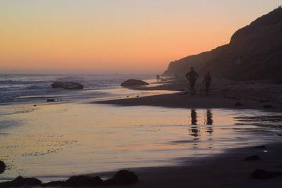 Silhouette man on beach against clear sky during sunset