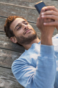 High angle view of man using mobile phone while lying on wooden pier