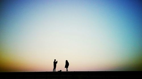 Silhouette people standing on landscape at sunset