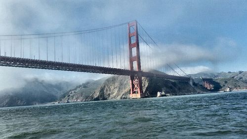 Suspension bridge over river against cloudy sky