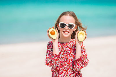 Portrait of girl holding avocado while standing at beach