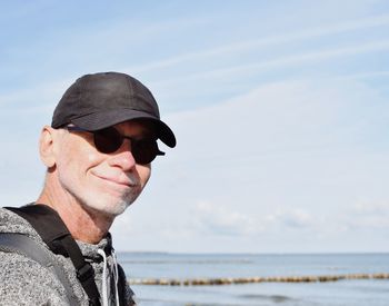 Portrait of man wearing sunglasses and cap at beach against sky