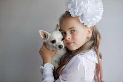 Portrait of cute girl holding chihuahua against gray background 