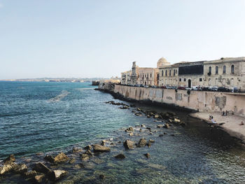 Buildings by sea against clear sky