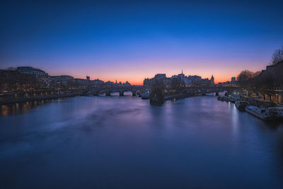 Bridge over river in city against sky at sunset