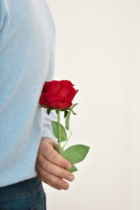Photo of man holding a red rose behind his back.