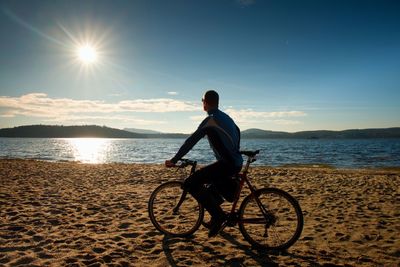 Young man cyclist sit on bike, blue sky and sunset background on beach. end of season at lake 