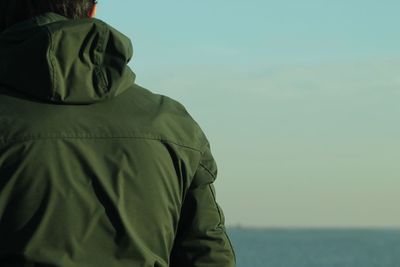 Midsection of man sitting by sea against sky