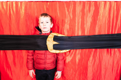 Portrait of cute boy standing against red curtain