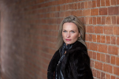 Portrait of young woman standing against brick wall