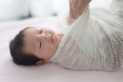 Cropped hand wrapping baby girl in net fabric on bed at home