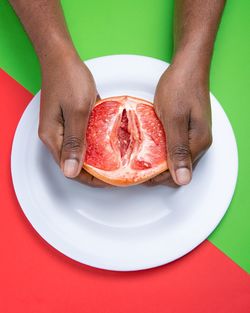 Cropped hands of person holding grapefruit in plate over two tone background