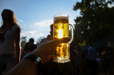 Close-up of hand holding beer glass against sky