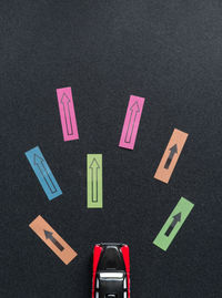 High angle view of toy car by colorful arrow symbols on black paper