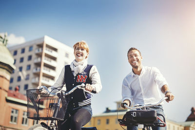 Happy business people riding bicycles in city against blue sky