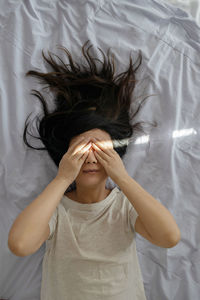 Portrait of young asian woman lying on bed at home on sunny day