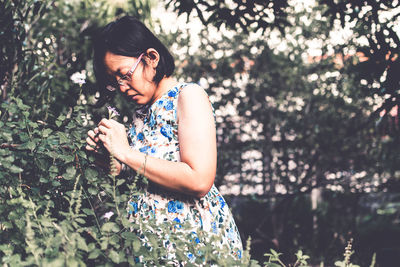 Woman smelling while standing by flowering plants