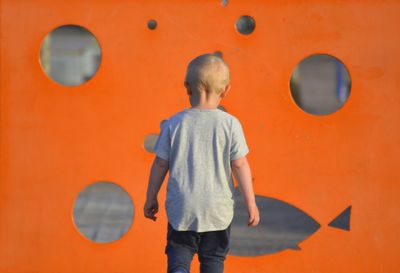 Rear view of boy standing against orange wall
