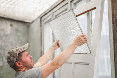 A young man removes corrugated glass from an old door.
