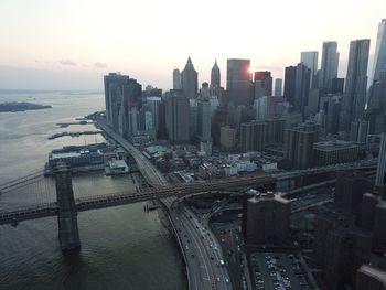 Bridge over river by buildings against sky during sunset