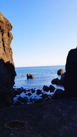 Rock formations in sea against clear blue sky