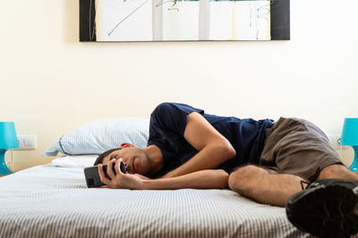 Man using phone while lying on bed at home