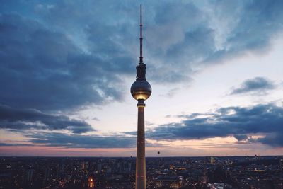 Fernsehturm against cloudy sky during sunset in city