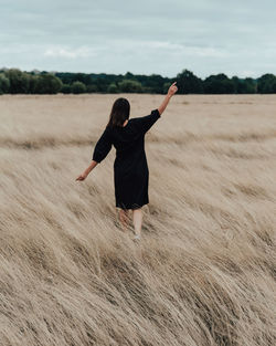 Rear view of woman standing with arms outstretched on land