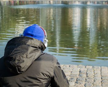 Rear view of man sitting by lake during winter