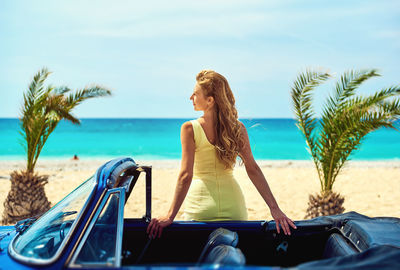 Rear view of woman standing by car against sea