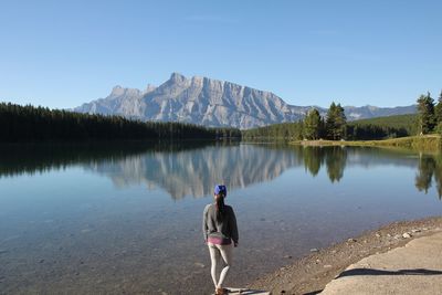 Rear view of man standing by lake against clear sky